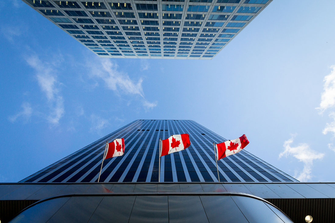 canadian flags at the bottom of downtown skyscrapers